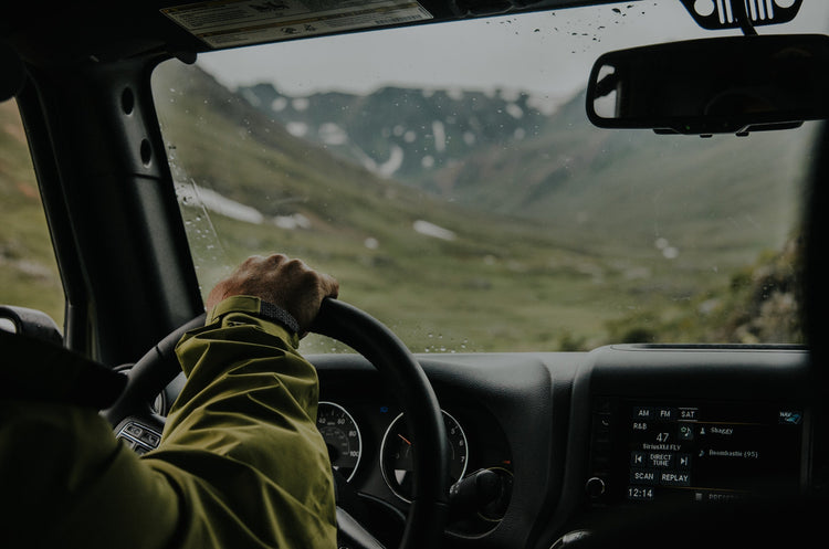 Man's hand of wheel of jeep with view out to mountains.
