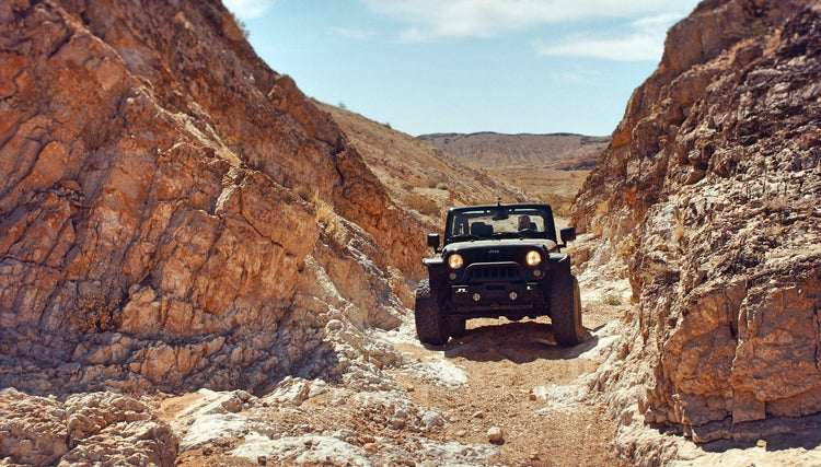 Jeep on dirt road in tight desert canyon.
