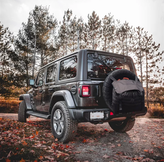 Jeep with Storage bag on rear tire in forrest.