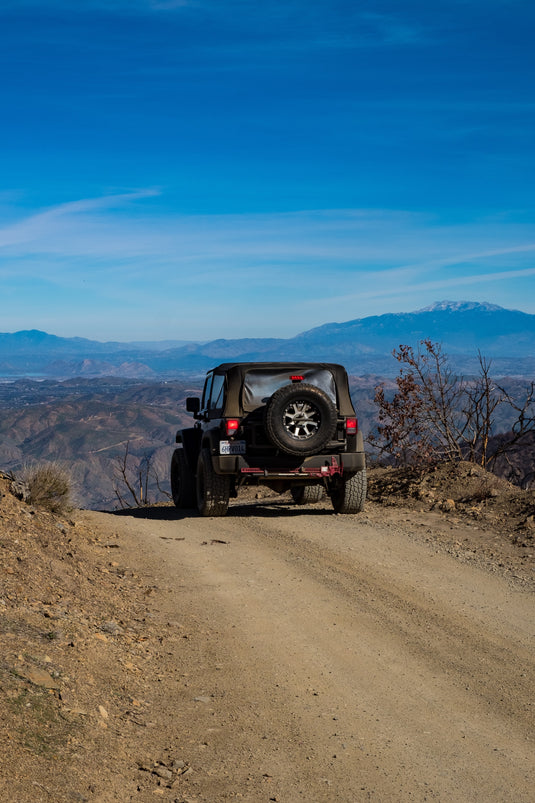 Jeep on dirt road, mountains and blue sky beyond. Photo by Daniel Salcius