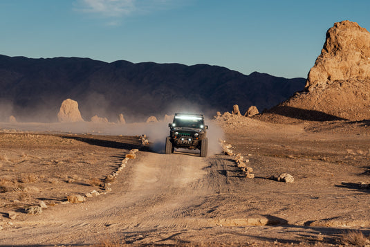 Jeep with lights on driving on dirt road through desert valley. Photo by Jeremy Bishop.