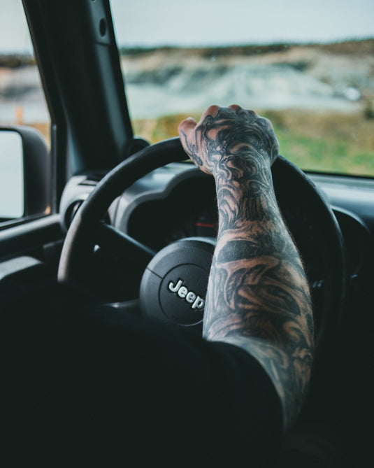 Man's arm with sleeve tattoo on Jeep steering wheel. Photo by Jonathan Cooper.
