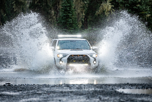 White 4runner moving quickly through a riverbed with off-road lights on. Photo by Kyle Grozelle
