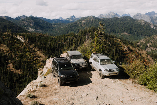 Three off road vehicles on promontory with mountains and forest valley beyond.