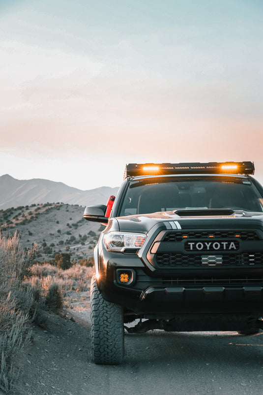 Truck with roof rack lights on, open dirt road with mountains beyond. Photo by Issac Mitchell